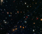 A dark background is dotted with galaxies of different shapes, sizes, and colors. There are red elliptical galaxies, blue spiral galaxies, and everything in between. This picture represents a snapshot of cosmic time in a particular part of the sky.