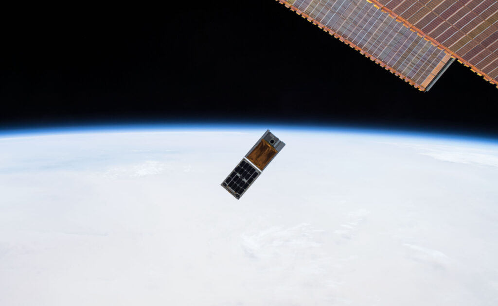 Photograph from the ISS showing two cubesats being deployed into orbit with Earth visible below.