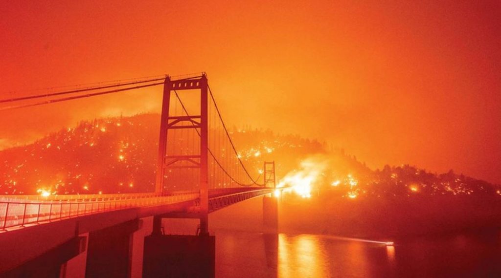 An eerie scene of the Golden Gate Bridge, with an orange sky backdrop, with raging fires in the background due to the California Wildfires.