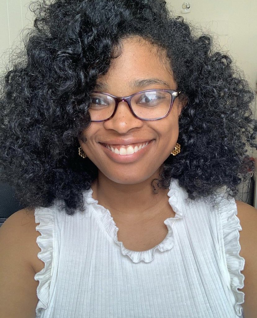 Photograph of Caprice Phillips, a Black woman wearing glasses and a white shirt, smiling at the camera.