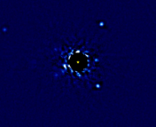 4 white dots representing exoplanets orbiting a central star with its light blocked out