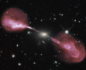 Composite photo of the radio galaxy Hercules A (the central bright spot) and its two prominent radio lobes (the reddish-pink clouds), imaged by the Hubble Space Telescope and the Very Large Array.