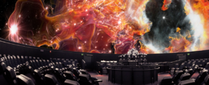 A photograph of the interior of a planetarium with an enormous domed screen that is currently showing a bright red and orange region of gas. Below the screen are rings of tilted-back chairs all facing a central podium.