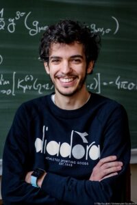 Paolo Cremonese smiling in front of a blackboard with physics equations