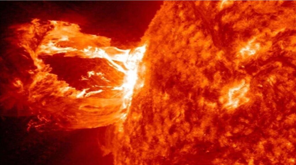 An image of a solar flare on the sun. The sun is a bright orange-red color and the flare appears as light escaping from it. The color is white at some points where the flare is leaving the sun. 