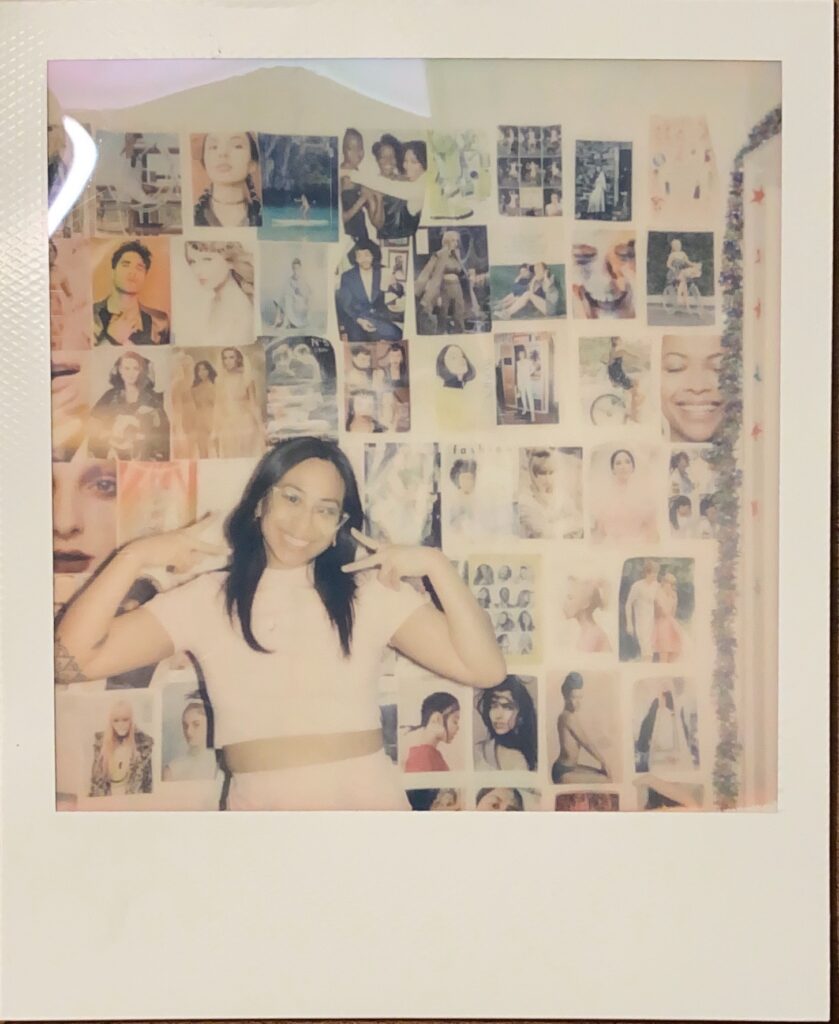 Polaroid of Teresa Panurach posed with peace signs in front of a collaged wall.