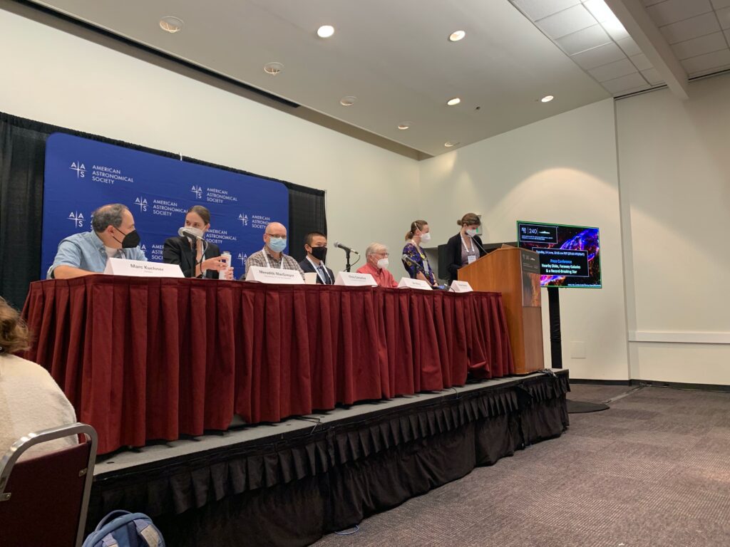 5 people behind a long table, all wearing masks, surrounded by screens and a formal AAS backdrop