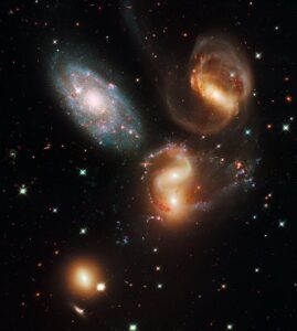 Hubble image of Stephan's Quintet, a visual grouping of five galaxies. Sparkling clusters of millions of young stars and starburst regions of fresh star birth grace the image. Sweeping tails of gas, dust and stars are being pulled from several of the galaxies due to gravitational interactions.