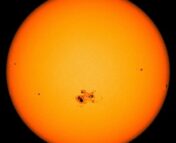 An image of sunspots on the Sun. An orange circle with a small dark region in the center.