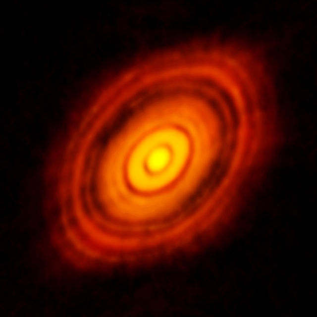 A bright central, yellow star, surrounded by concentric ellipses in red on a black background.  