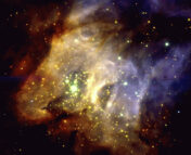 A broad, amorphous shape of gas and dust, colored in shades of gold and brown from reddish to blueish, makes up the entirety of the image. Many stars of various colors populate the center of the region in clusters.