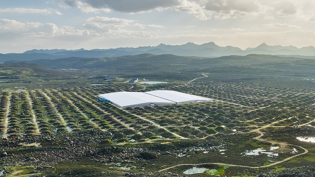 wide angle view of lhaaso. there are many mounds of dirt which house sensors, surrounding two large white buildings in the center