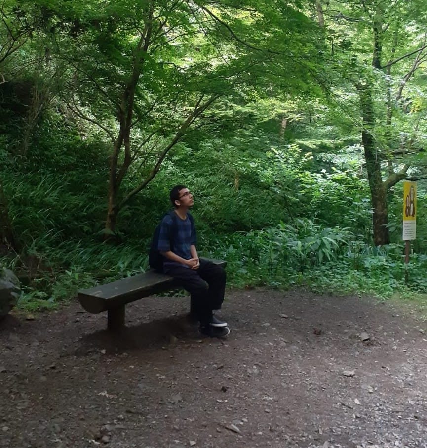 A photo of the author. He appears to be sitting on a bench in the forest, looking away from the camera.