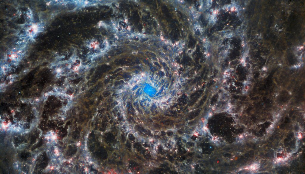 The galaxy contains delicate filaments of gas and dust in the grandiose spiral arms which wind outwards from the center of this image. A lack of gas in the nuclear region also provides an unobscured view of the nuclear star cluster at the galaxy's center.