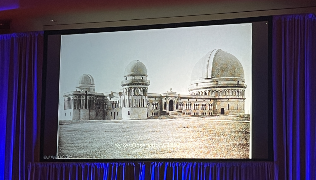 An image of one of the slides from Sam Hale's AAS 244 plenary. The slide is an images of Yerkes observatory from when it first opened in 1987. It features three large telescope domes attached tp the same building, with a large lawn in the foreground. An image caption reads "Yerkes Observatory 1897". Credit: Sam Hale