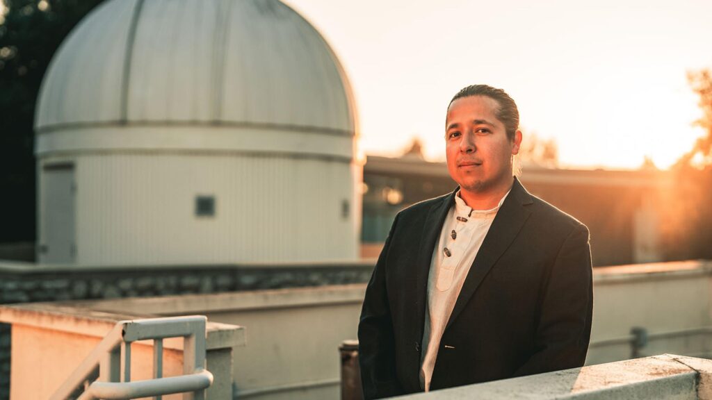 A man standing in front of a telescope dome at sunset