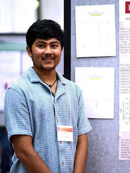 Vidit standing in front of a poster at a conference.