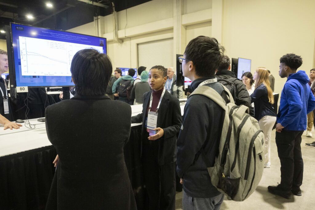 Logan presenting in front of a virtual poster at AAS to two other meeting attendees.