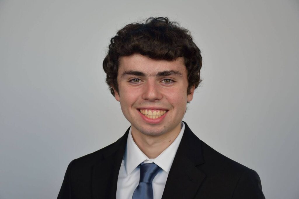 photo of a person in a suit and blue tie smiling at the camera