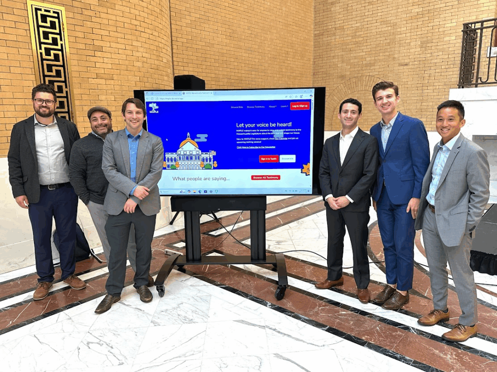 6 men in suits standing around a screen at the Massachusetts state house.