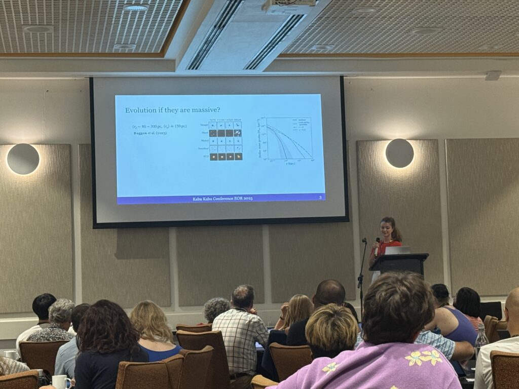 Josephine Baggen stands at a podium giving a talk with a slide titled “Evolution if they are massive?” The slide includes image panels for four objects showing images, mask, model, residual, RGB from top to bottom and a graph comparing size in kpc and stellar mass profile for LRDs.