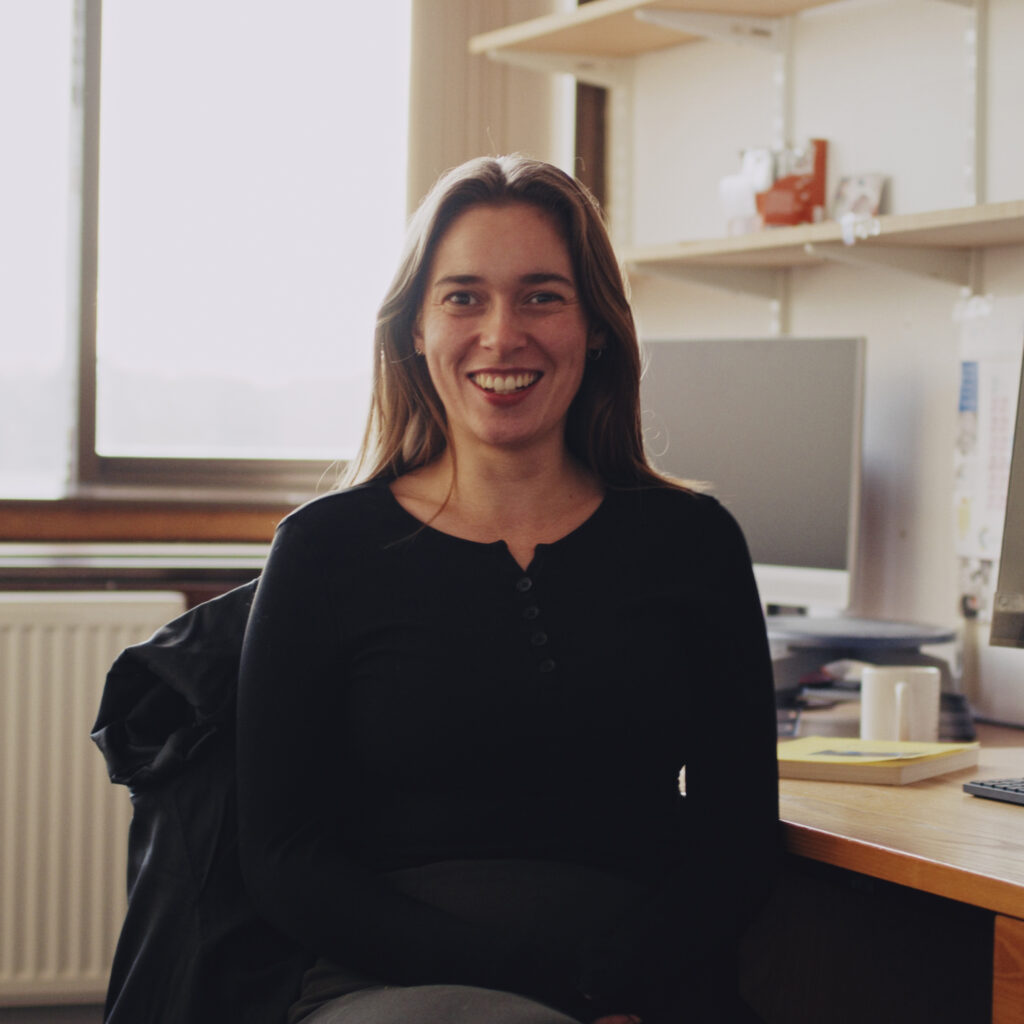 Tibby Finn Leeming sits at her desk, smiling at the camera. 